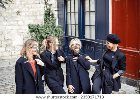 Portrait of group of young laughing wonderful women friends with fair hair wearing black clothes, standing outside on street near colored red blue walls, conversing interacting sneering making jokes. Royalty-Free Stock Photo #2350171713