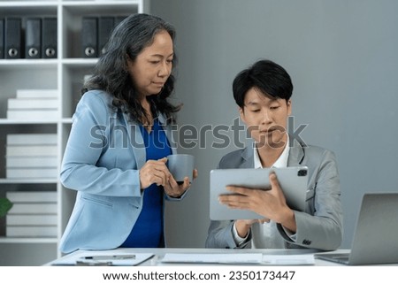 senior asian business woman Discuss and advise Consulting young office workers about marketing plans, paperwork, financial information from the tablet to analyze and summarize the work in the office
