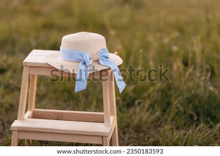In the summer green field there is a wooden stool on which lies a hat with a blue ribbon, the concept of the summer season. High quality photo