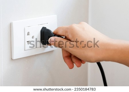 Hand holding plug connect to a power plug into a electrical outlet on a wall, power outlet socket, power saving concept, energy saving, energy conservation. Royalty-Free Stock Photo #2350184783