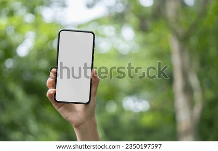 Girl holds in her hand a smartphone close-up, with a white screen against the backdrop of the blurred of nature. Mock-up Technology