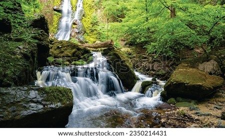 The waterfall is surrounded by lush green trees and rocks. The water is cascading down the rocks in a beautiful stream. The image is very serene and peaceful.