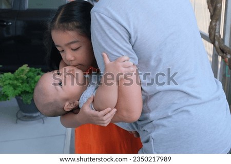 Pretty little girl kissing his young baby brother in her grandma's arms
