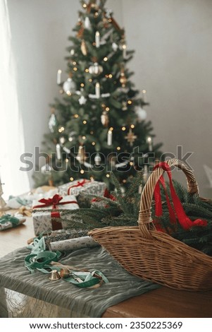 Rustic basket with fir branches, stylish christmas gifts and festive decorations on table on background of beautiful vintage christmas tree and fireplace. Merry Christmas and Happy Holidays!