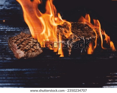 Beef steak on the grill, surrounded by flames.
