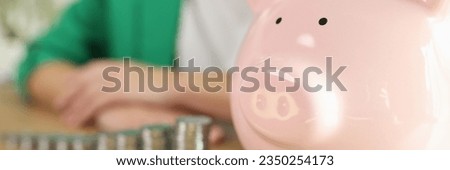 Piggy bank and stacks of coins on wooden table, business person in background. Saving money, control income and smart investment concept.