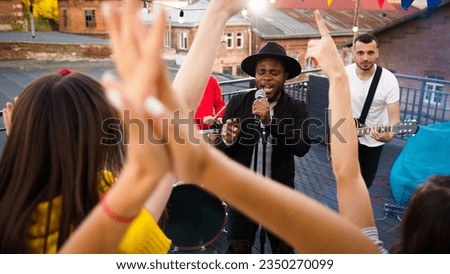 Band with guitarist, drummer and singer performing at a concert on party. Group of friends hanging out, enjoying rooftop event at sunset, dancing and listenin to music.