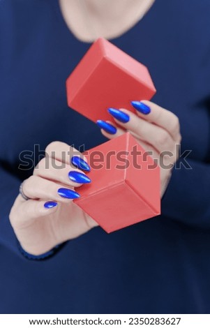 Female hands with blue long nails hold a gift box in red colors