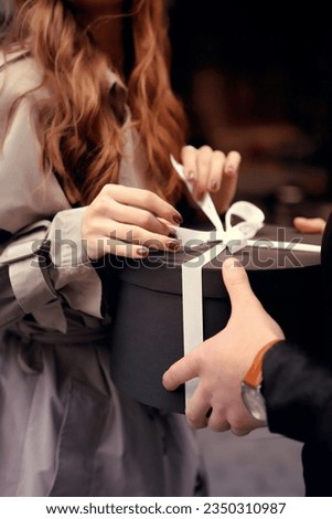 Hands of a couple with a gift present. Man gives a present with a white ribbon to his girlfriend on the street. Woman takes a gift from her boyfriend. Valentines day and Christmas concept.
