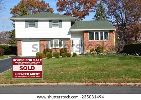 Sold real estate (another success let us help you buy sell your next home) sign Suburban Brick High Ranch home autumn day residential neighborhood clear blue sky USA