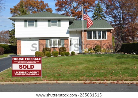 American flag pole sold real estate (another success let us help you buy sell your next home) sign Suburban Brick High Ranch home autumn day residential neighborhood clear blue sky USA