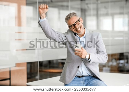 Lucky mature businessman holding a cellphone and celebrating success. Middle aged male ceo, trader, investor reading good news on a smartphone online, winning on the stock market, raising fist up