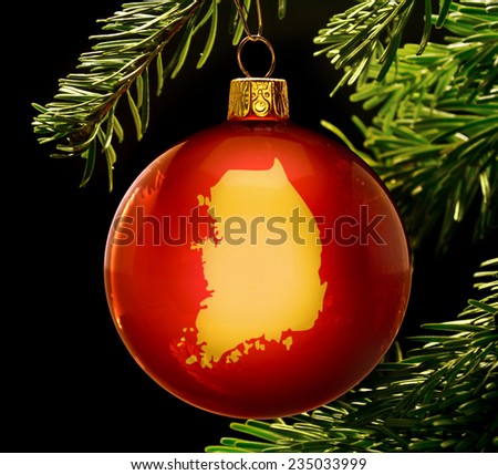 A red bauble with the golden shape of  South Korea hanging on a christmas tree isolated on black.(series)