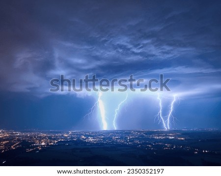 Spectacular, aerial shot of a city hit by multiple lightning. Dramatic, real drone shot of a massive storm over city. Lightning between the clouds and the ground. Blue and purple colors. Royalty-Free Stock Photo #2350352197