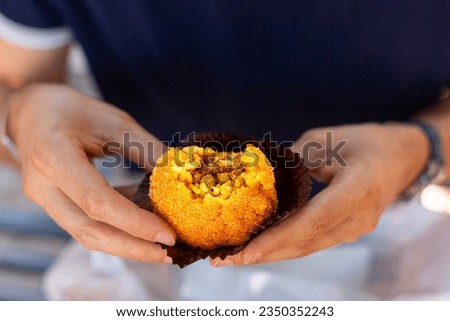 A man eating arancini, italian rice ball al ragu or al sugo, that is stuffed  with meat, peas and tomato sauce and spices, coated with breadcrumbs and deep fried. Sicilian street food, cuisine.  Royalty-Free Stock Photo #2350352243