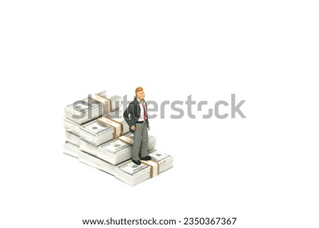 Miniature tiny people toy figure photography. Business failure concept. A businessman standing above declining paper money staircase. Isolated on a white background. Image photo Royalty-Free Stock Photo #2350367367