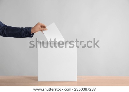 Woman putting her vote into ballot box on wooden table against light grey background, closeup. Space for text Royalty-Free Stock Photo #2350387239