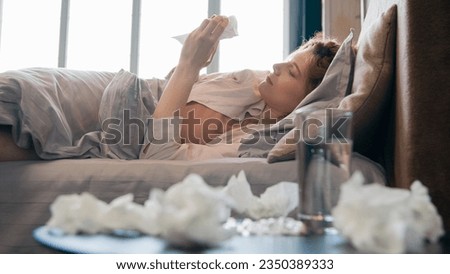 Caucasian ill upset sick unhealthy unwell woman blowing running nose sickness girl flu cold sneezing in tissue lying in bed health problem flue allergy symptoms holding napkin throw away in bedroom Royalty-Free Stock Photo #2350389333