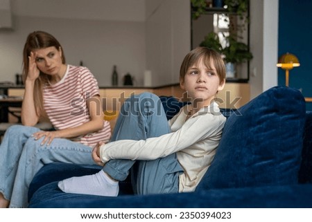 Quarrel between mother and child, resentment, ignoring. Upset teenage boy looks away, hugging legs avoiding contact with disgruntled angry mama. Tensions situation in family between mom and son. Royalty-Free Stock Photo #2350394023