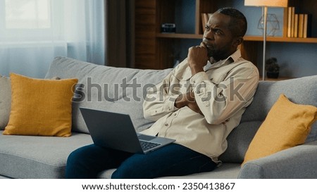 Thoughtful puzzled african american man businessman freelancer working on laptop at home couch think about solving business problem serious pensive male searching inspiration for new ideas thinking Royalty-Free Stock Photo #2350413867
