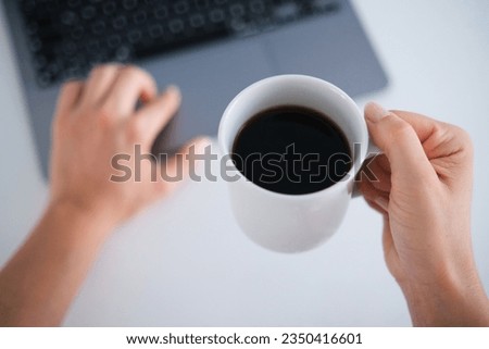 Top view young woman's holding a cup of filter coffee while using laptop.Daily routine, morning person.Coffee day concept.
