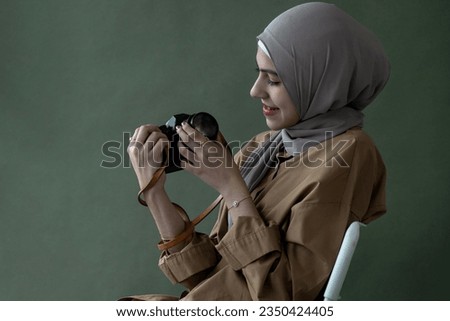 Pretty Muslim girl in hijab holding vintage camera over background in studio, check the neatness of the camera