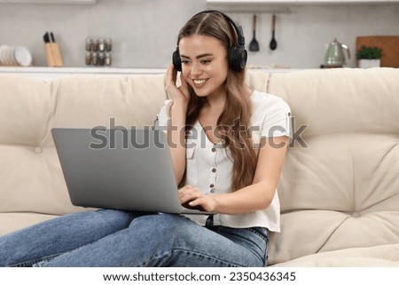 Happy woman with headphones and laptop on couch in room