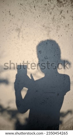 Sunlight Casts a Black Shadow on the Wall of a Person Holding a Smartphone and Shadows from a Tree