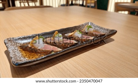 Japanese food menu of tuna tataki with soy sauce served on a wooden table.