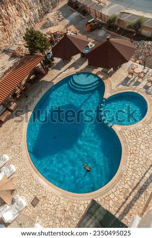 Aerial shot of a swimming pool with a woman bathing enjoying the summer vacation