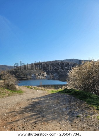 view of Bovan lake in spring, blue water above it, blue sky, grass, dirt road and some trees, wilderness