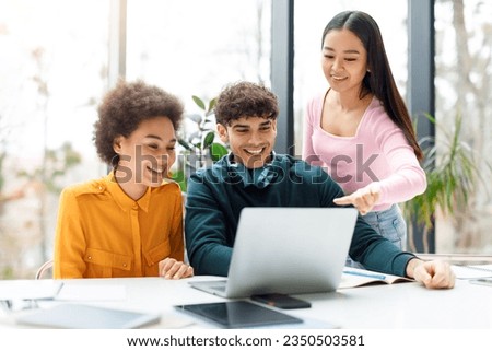 Cheerful diverse students sitting at desk in audience and using laptop computer, making project together and discussing or watching educational video
