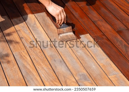 Woodworker refreshing wooden floor, worker's hand is applying decking oil on deck with a painting brush after sanding Royalty-Free Stock Photo #2350507659