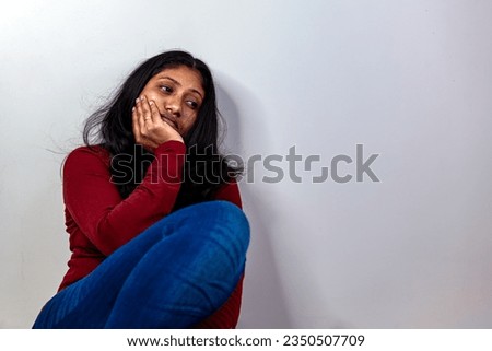 A sad woman sits with her hand on her chin, looking lost in thought Royalty-Free Stock Photo #2350507709