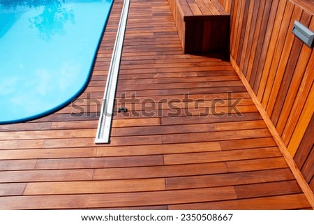 Ipe wood deck and swimming pool edge. Poolside decking design close up, horizontal and vertical wooden cladding structure, blue water contrasting with exotic hardwood boards