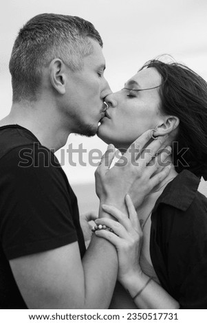 A young couple of beautiful people have fun in the field near round bales of dry hay. A man kissing his wife near a bale of straw. Black and white image. Royalty-Free Stock Photo #2350517731