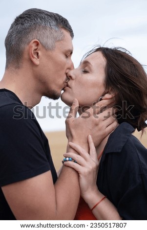A young couple of beautiful people have fun in the field near round bales of dry hay. A man in a black T-shirt and jeans kiss a girl in a black shirt and an orange dress near a bale of straw. Royalty-Free Stock Photo #2350517807