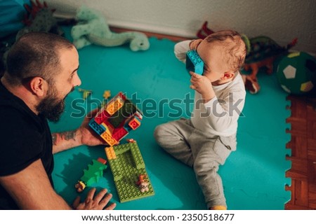 Fun father is entertaining his boy during his playtime at home while babysitting a boy. A happy family playing together at home. Healthy development and upbringing. Father is playing with his son. Royalty-Free Stock Photo #2350518677