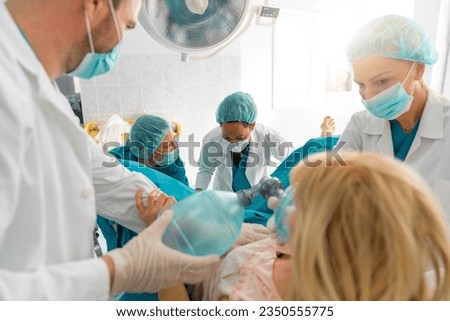 Group of medical professionals helping pregnant woman to deliver baby, giving her oxygen and encouraging her in hospital delivery room. Medical team and pregnant woman in labor.