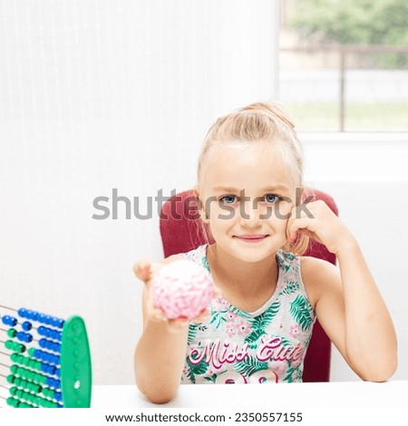 Beautiful little girl sits at her writing desk and holds a toy brain in her hand. Back to school concept 