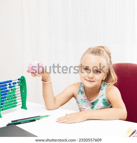 Cute blonde girl sitting at her desk at home and holds a toy brain. Back to school concept	