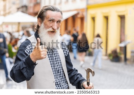 Like. Happy bearded senior old man looking approvingly at camera showing thumbs up sign positive something good positive feedback. Elderly mature grandfather standing in urban city sunshine street