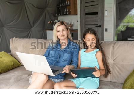 mother and daughter with laptop and tablet on sofa
