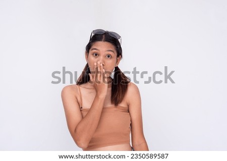 A mildly surprised young filipino woman with eyebrows raised covering her mouth with one hand. Reacting to scandalous gossip or expose. Isolated on a white background. Royalty-Free Stock Photo #2350589587