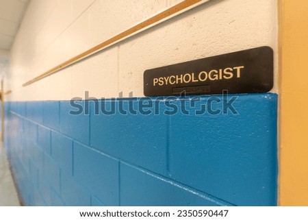 Psychologist Office, counselor office, sign with braille, on a white and blue wall at door to school office.	