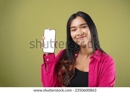 Photo of of cheerfull Asian woman holding smartphone mockup of blank screen and smiling on green pastel background.