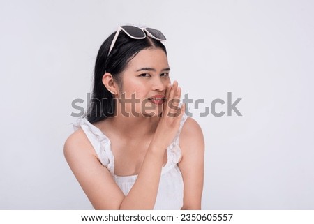 A loquacious young asian woman leans forward, sharing some secrets in a discreet way. Isolated on a white background.