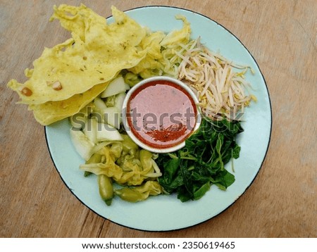  In the form of several vegetables such as spinach, bean sprouts, cucumber, turi flowers and chicory mixed with peanut sauce. Boiled vegetables are placed on a plate. Indonesian food. Top view.