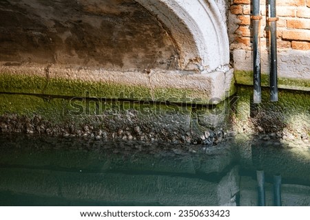 Photo of part of the concrete footing of a brick building and it's reflection in the water in a canal in Venice, Italy.