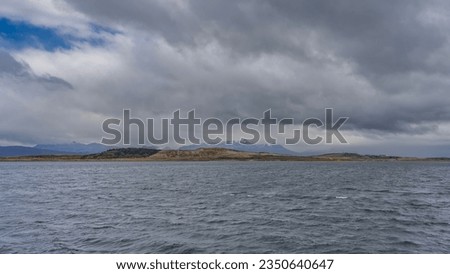 Hills and mountains against a background of blue sky and clouds. Ripples on the blue water of the strait. View from the Beagle Canal on the coast of Argentina. Tierra del Fuego archipelago.